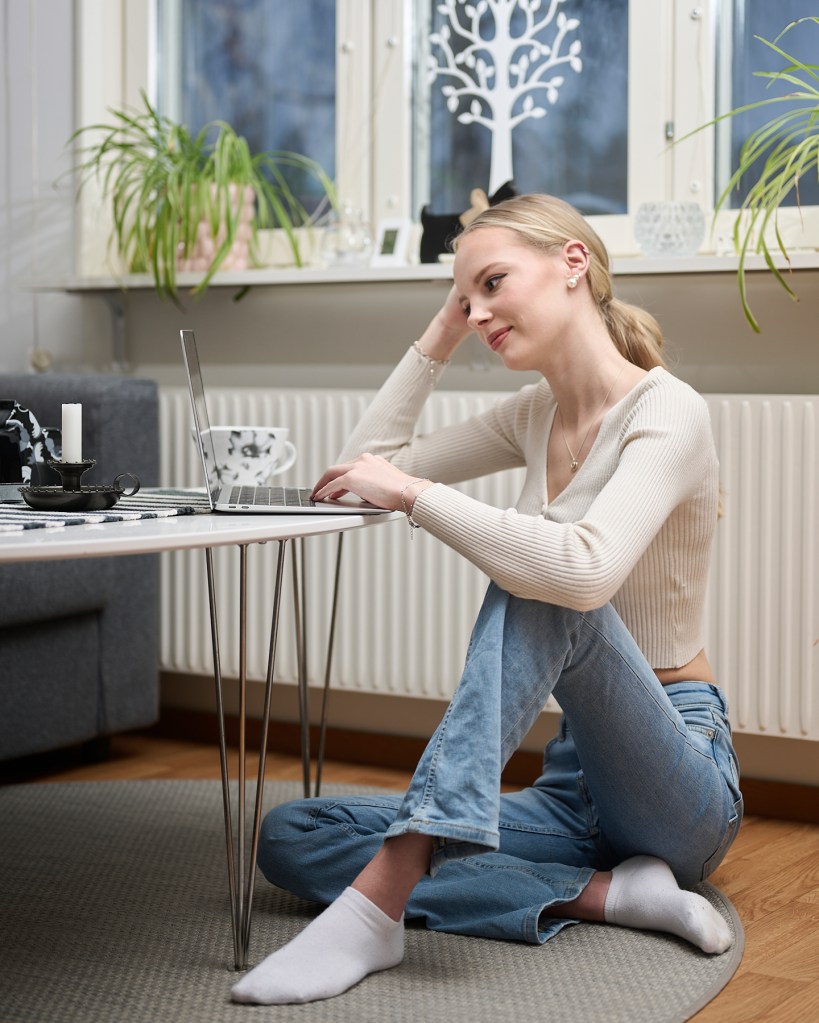 kvinna sitter på gilvet med datorn på bordet och arbetar