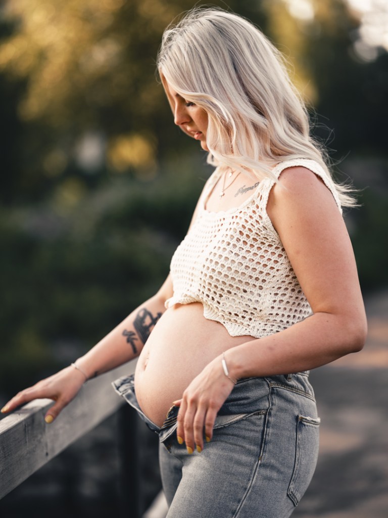 nätlinne, gravidmage och jeans ute på en bro