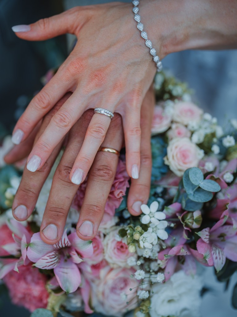 Håller upp bröllopsbuketten och visar sina ringar ovanpå blommorna