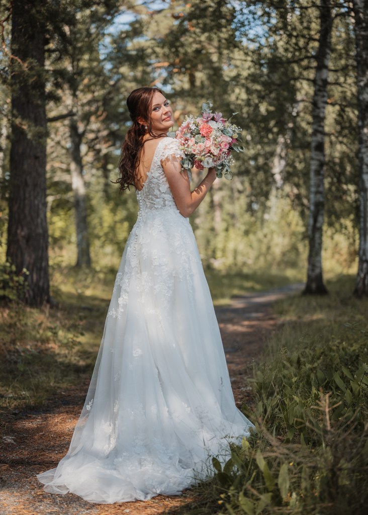 Brudporträtt i skogen, fokus på klänningen och blommorna, tittar sig över axeln mot mig