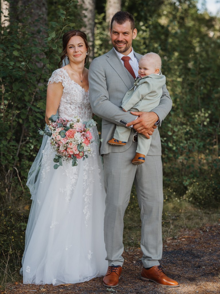 Brudparet står i skogen och håller i sitt barn. klassiskt porträtt