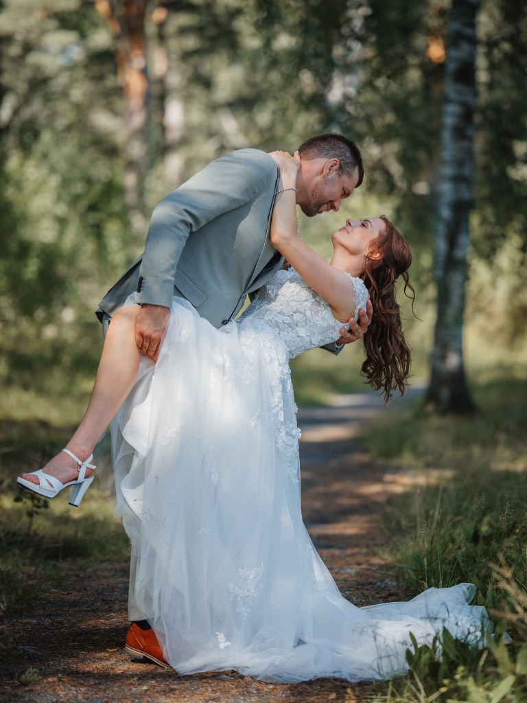Brudparet dansar i skogen, han håller upp hennes ben så man ser skon.