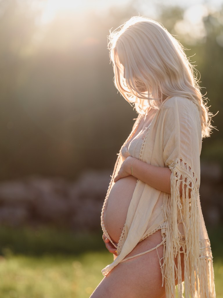 gravid står i motljus vid solnedgång